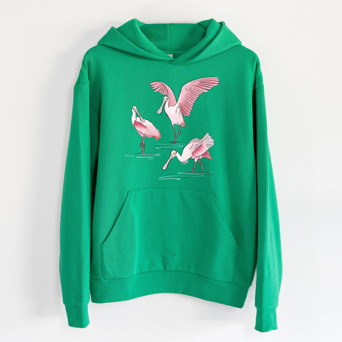 Roseate Spoonbill Trio - Platalea ajaja - Statement Midweight Hoodie in Kelly Green, hanging on a white wall, with a front kangaroo pocket and no drawcords.