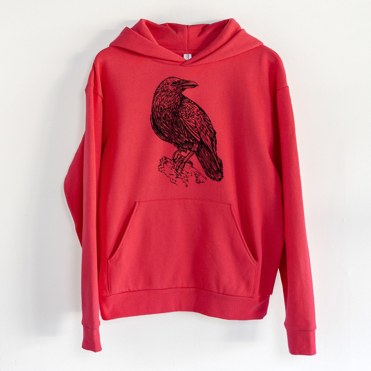 Corvus corax - Common Raven - Statement Midweight Hoodie in Cherry Red, hanging on a white wall, with a front kangaroo pocket and no drawcords.