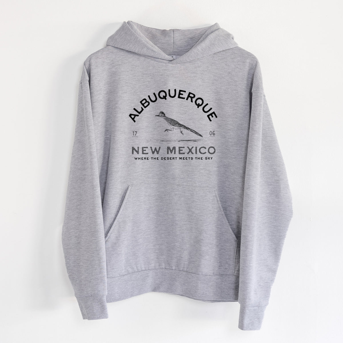 Albuquerque New Mexico Roadrunner - Statement Midweight Hoodie in Heather Grey, hanging on a white wall, with a front kangaroo pocket and no drawcords.