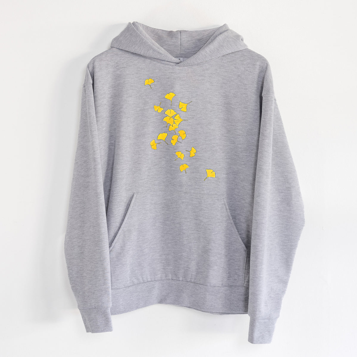 Falling Ginkgo Leaves - Statement Midweight Hoodie in Heather Grey, hanging on a white wall, with a front kangaroo pocket and no drawcords.