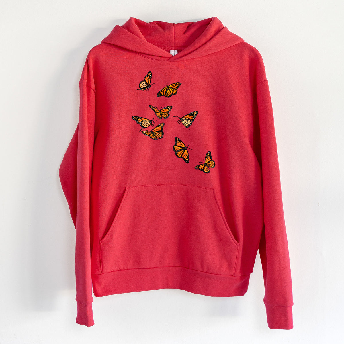 Monarch Migration - Statement Midweight Hoodie in Cherry Red, hanging on a white wall, with a front kangaroo pocket and no drawcords.