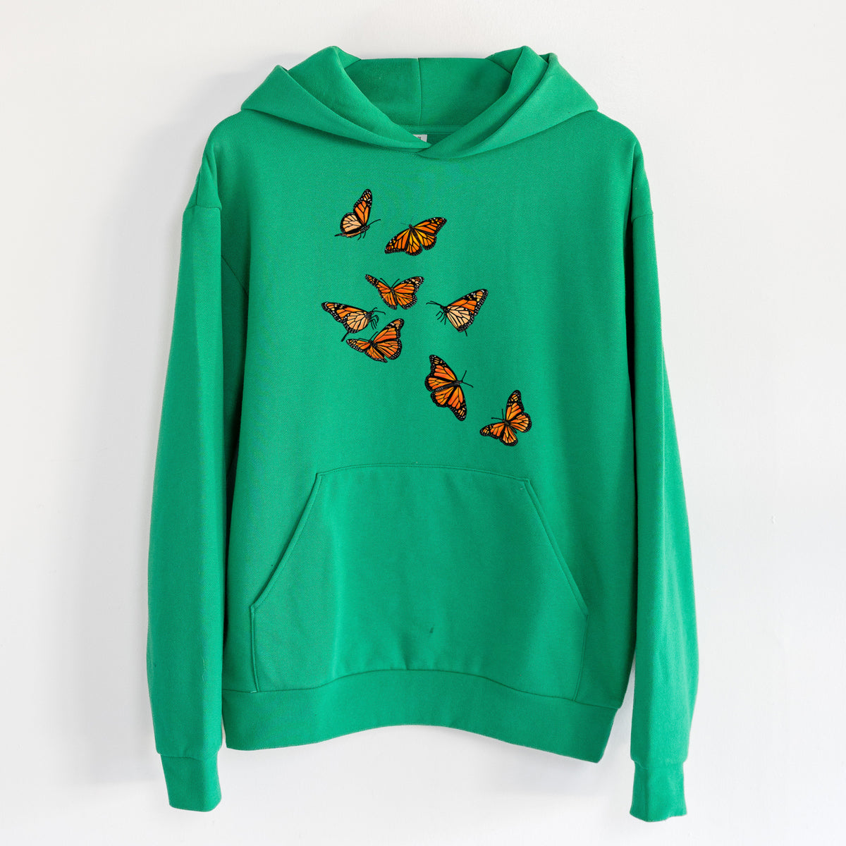 Monarch Migration - Statement Midweight Hoodie in Kelly Green, hanging on a white wall, with a front kangaroo pocket and no drawcords.