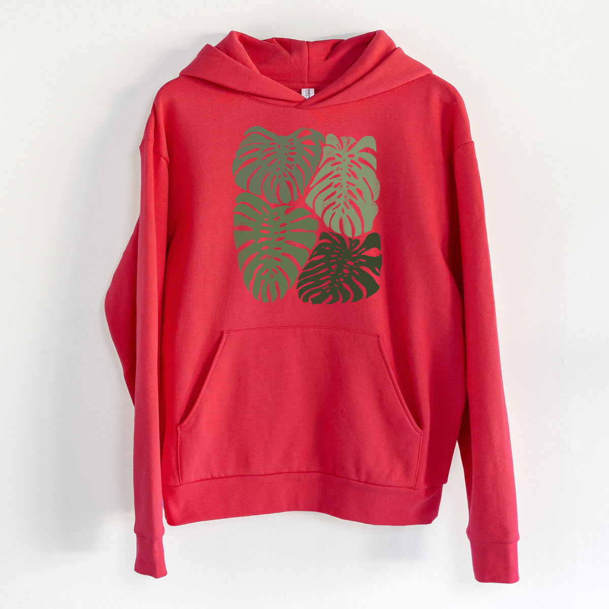 Monstera Vibes - Statement Midweight Hoodie in Cherry Red, hanging on a white wall, with a front kangaroo pocket and no drawcords.