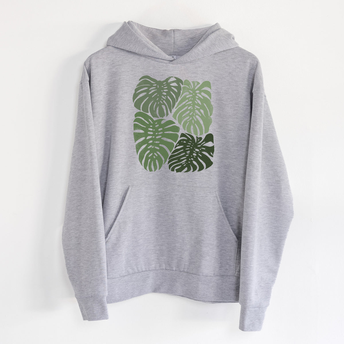 Monstera Vibes - Statement Midweight Hoodie in Heather Grey, hanging on a white wall, with a front kangaroo pocket and no drawcords.