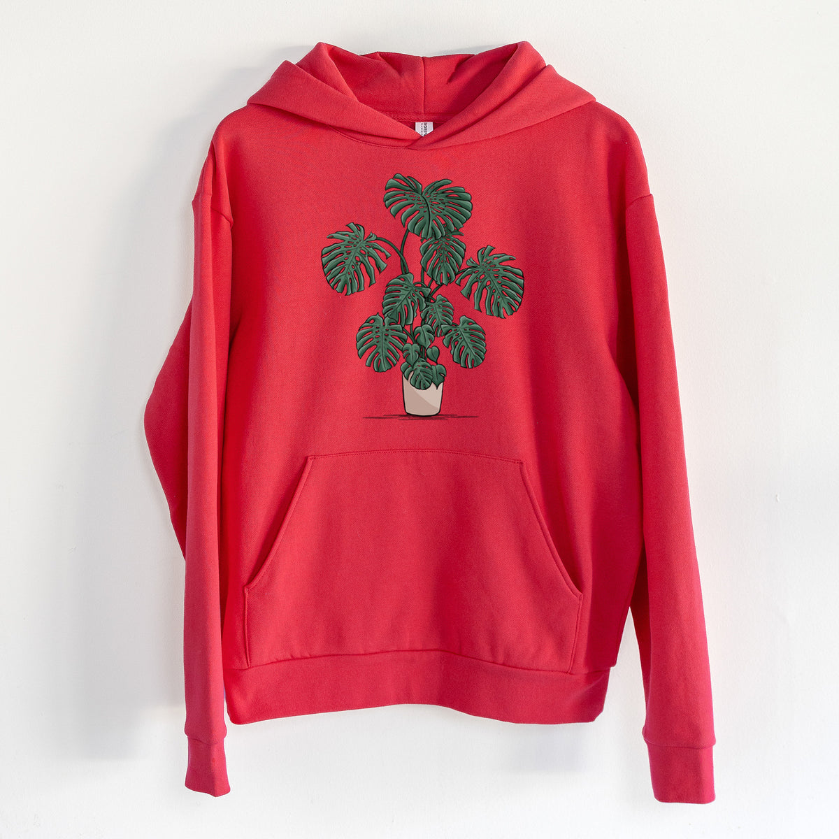 Potted Monstera Plant - Statement Midweight Hoodie in Cherry Red, hanging on a white wall, with a front kangaroo pocket and no drawcords.