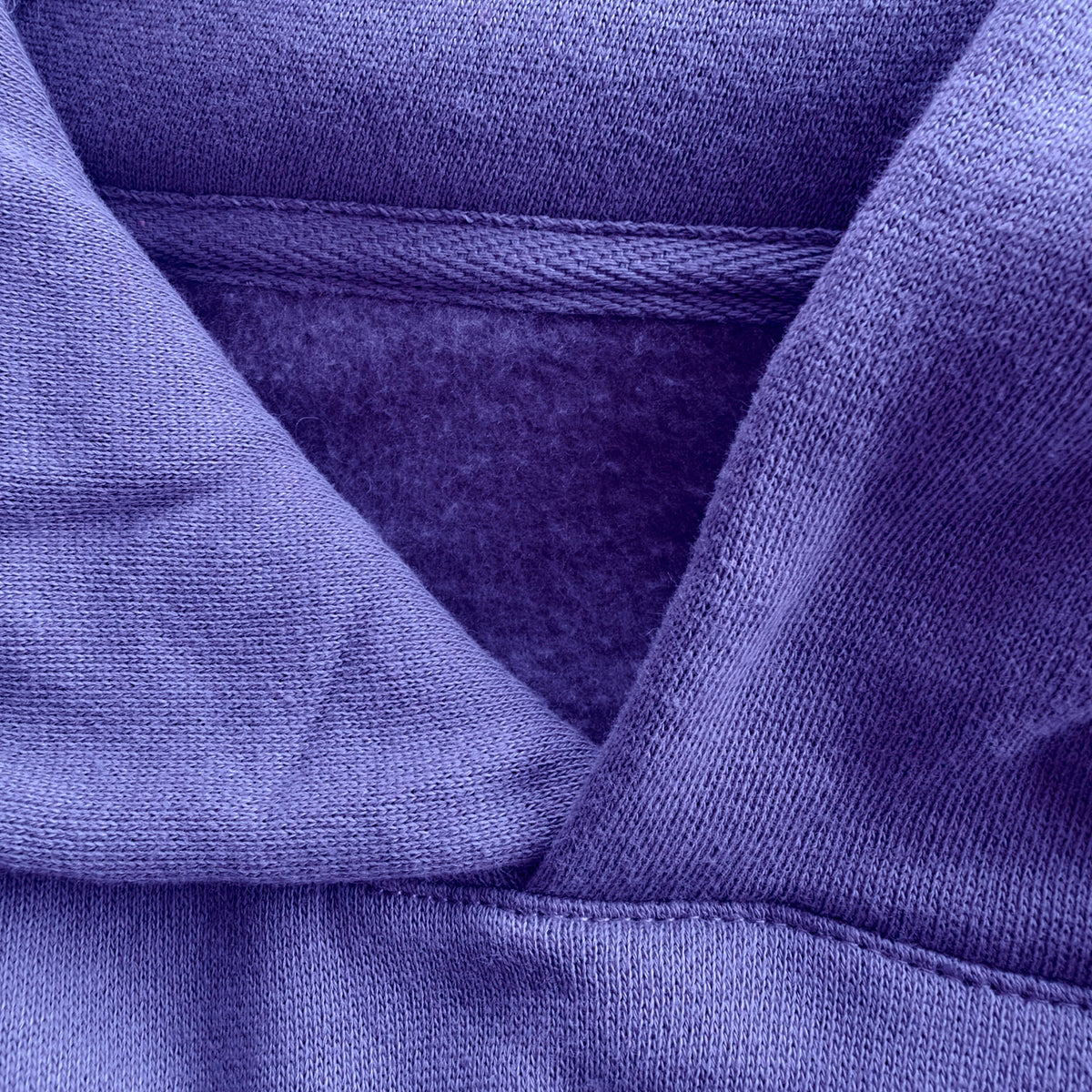 Close-up of the violet Statement Hoodie, showing the hood seam, herringbone neck tape and soft brushed fleece interior.