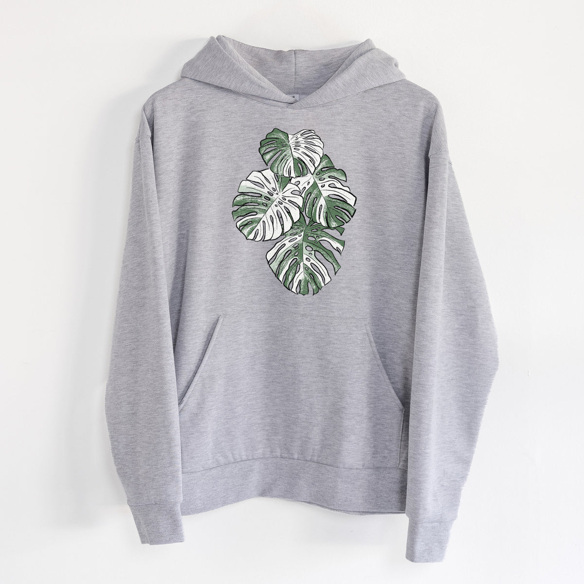 Variegated Monstera - Statement Midweight Hoodie in Heather Grey, hanging on a white wall, with a front kangaroo pocket and no drawcords.